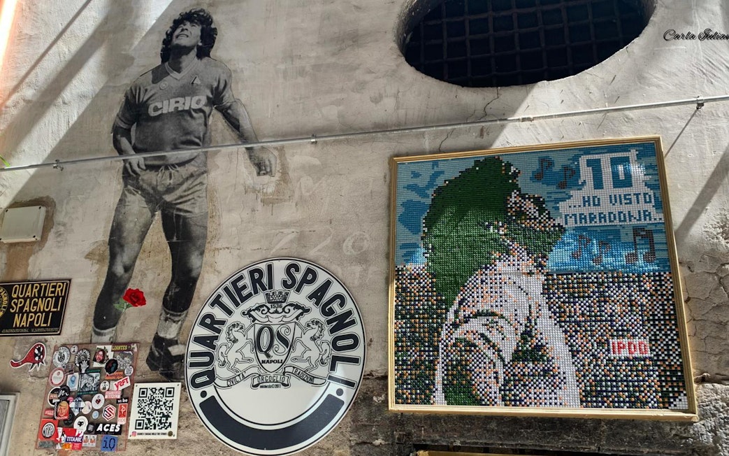 Mural of Diego Maradona in Quartieri Spagnoli, Naples, with mosaic art and local street signs.