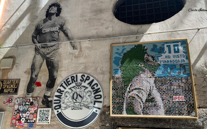 Mural of Diego Maradona in Quartieri Spagnoli, Naples, with mosaic art and local street signs.