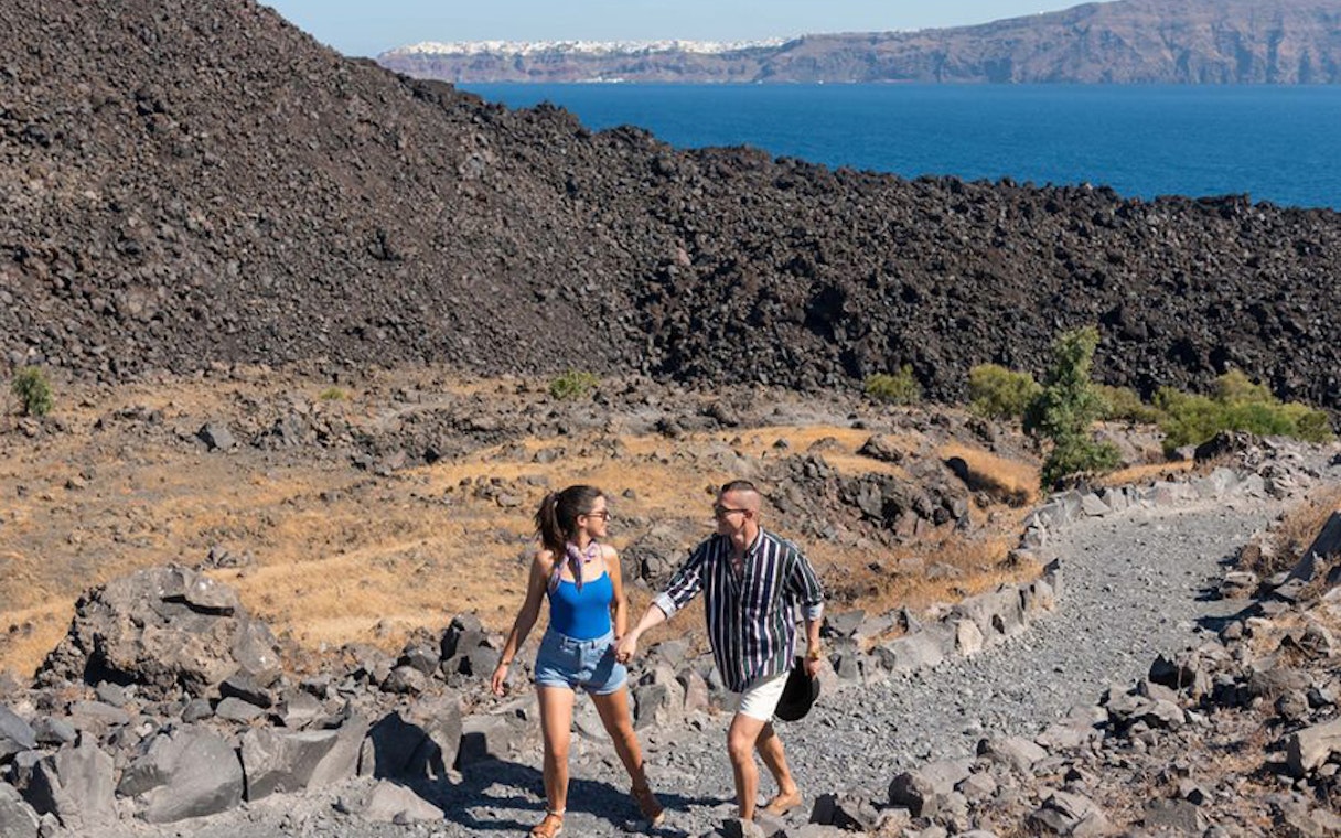 Couple hiking on rocky path with sea view during Santorini sightseeing tour.