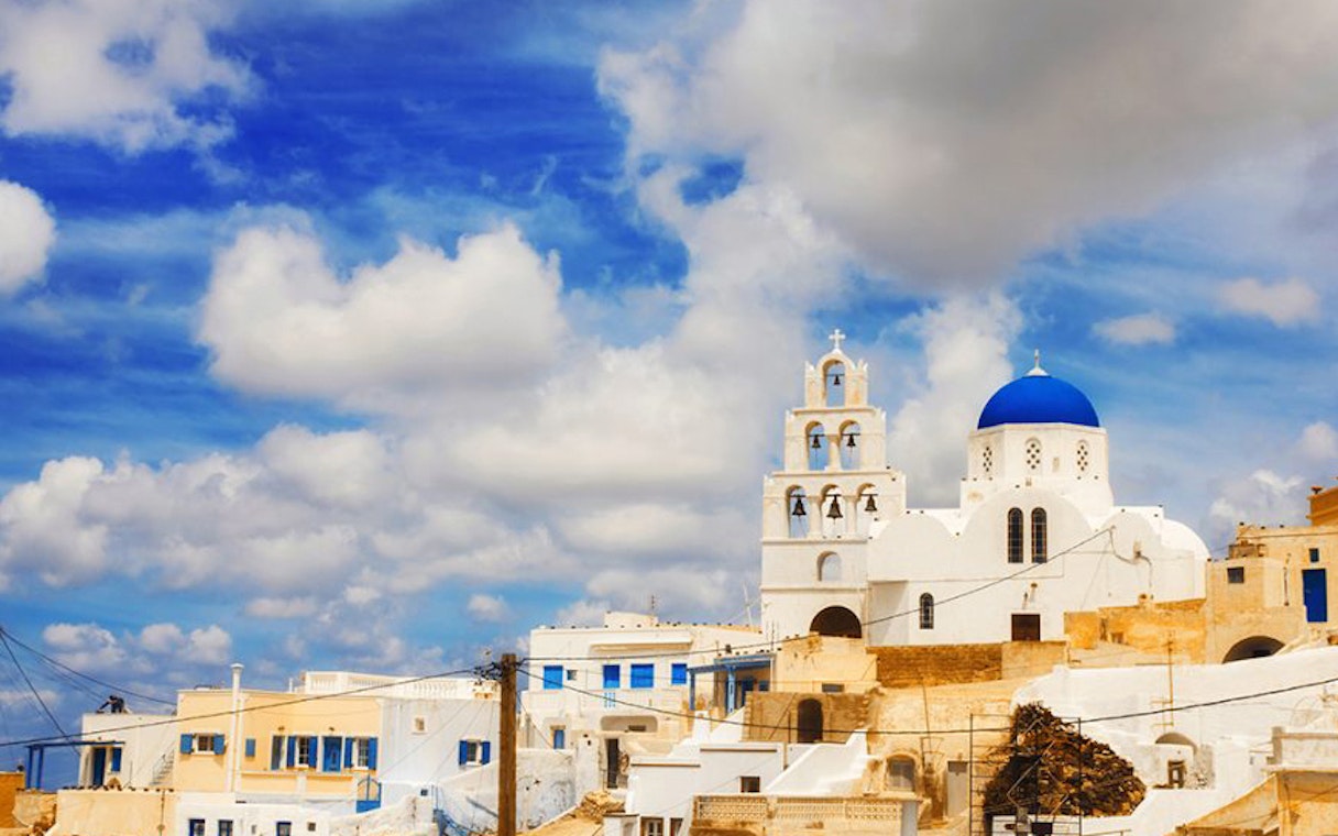 White buildings with blue domes in Santorini under a cloudy sky.