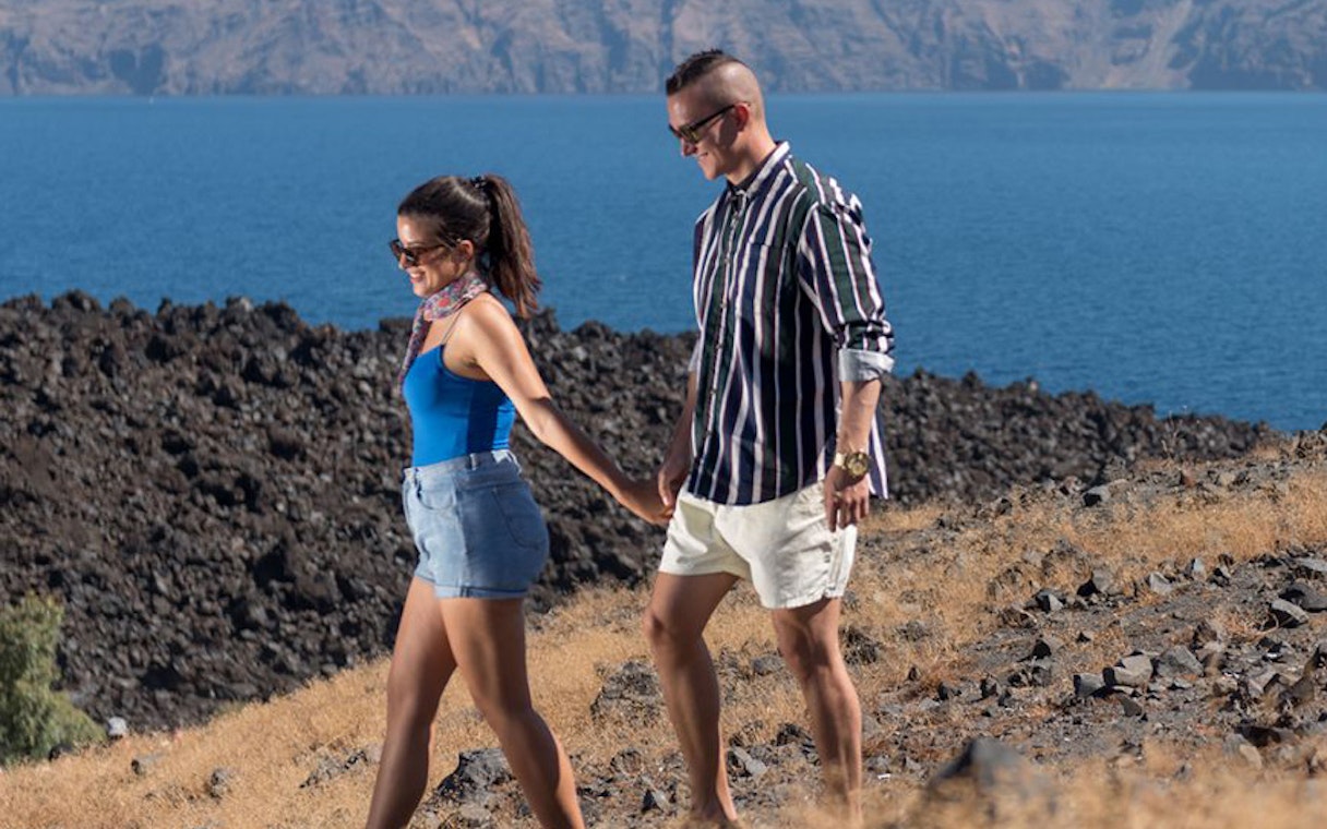 Couple walking on rocky terrain with Santorini caldera view.