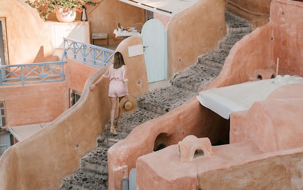 Woman walking up stone steps in Santorini, Greece, with traditional architecture.