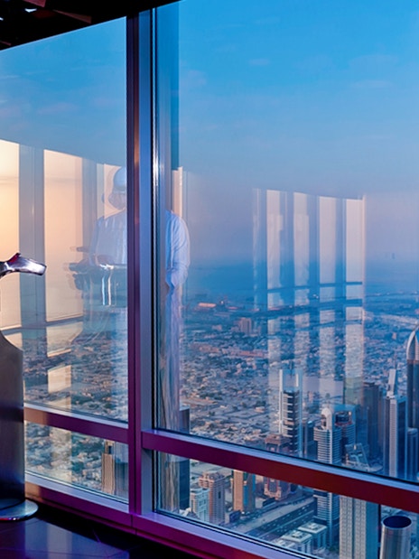 Man using telescope at Burj Khalifa observation deck, overlooking Dubai skyline.