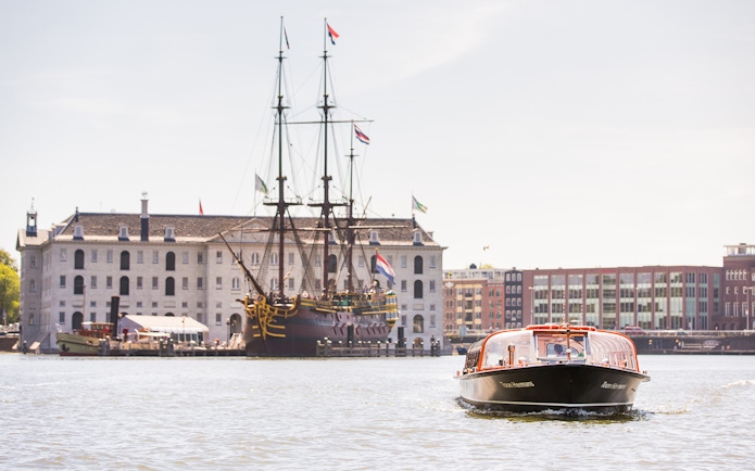 Amsterdam canal cruise boat near NEMO Science Museum with historic ship in background.