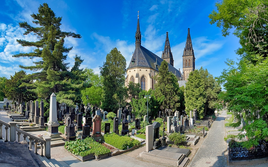 Vyšehrad Castle cemetery with church spires and surrounding greenery in Prague.