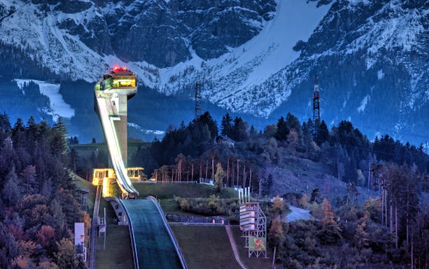 Bergisel Ski Jump Stadium illuminated at dusk with mountain backdrop in Innsbruck, Austria.
