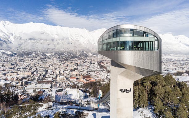 Bergisel Stadium ski jump tower overlooking Innsbruck with snowy mountains in the background.