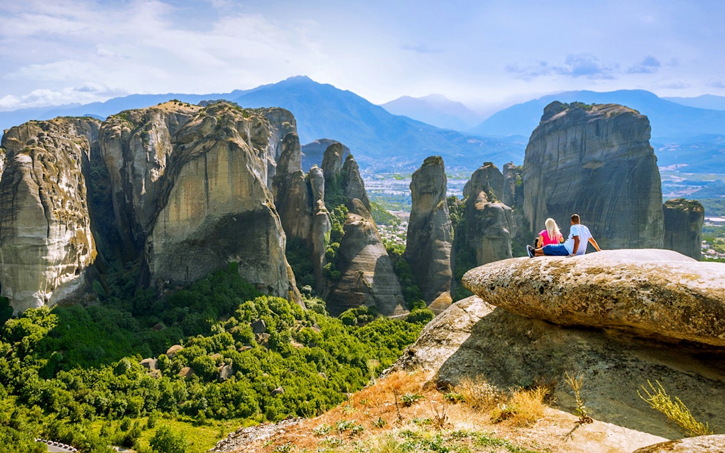 Couple sitting on rock overlooking Meteora rock formations, Greece.