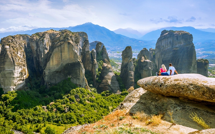 Couple sitting on rock overlooking Meteora rock formations, Greece.