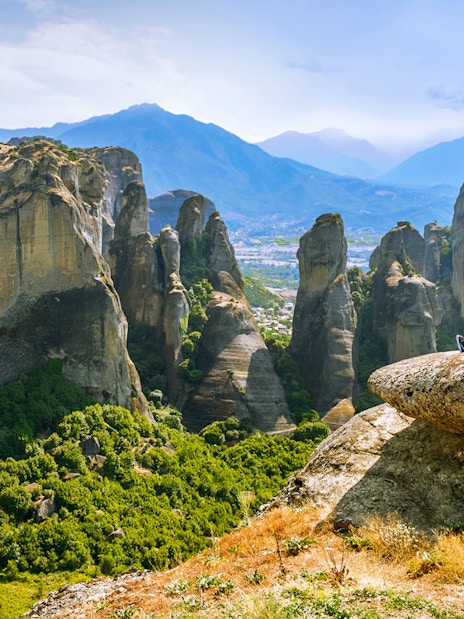 Couple sitting on rock overlooking Meteora rock formations, Greece.