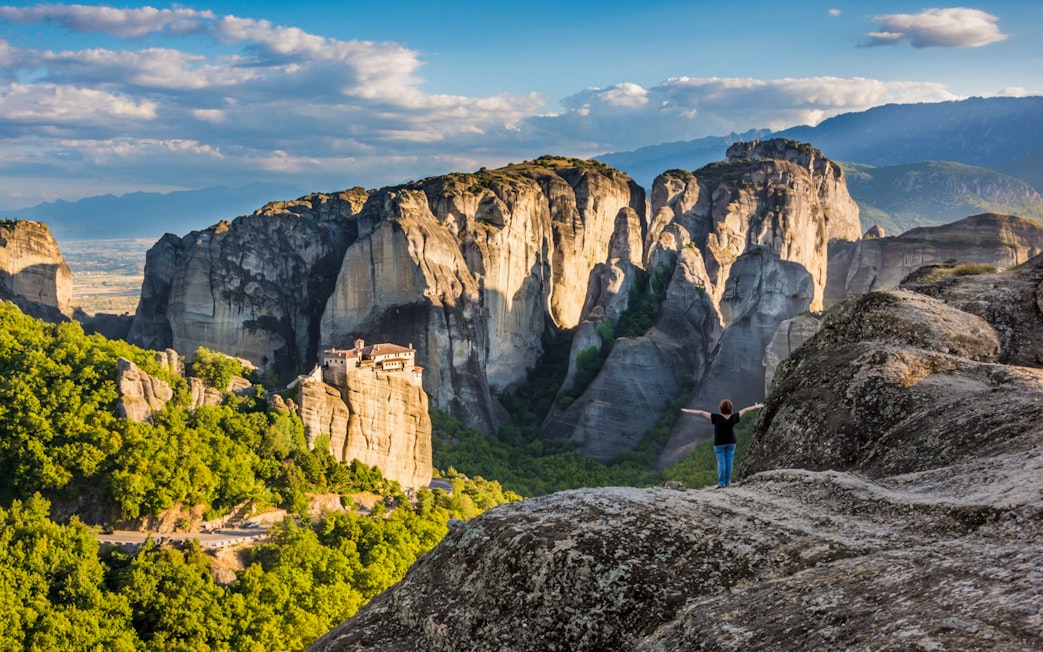 Meteora rock formations with monastery, person standing on cliff, Greece.
