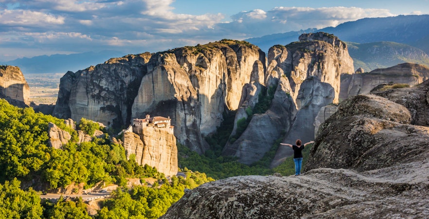 Meteora rock formations with monastery, person standing on cliff, Greece.
