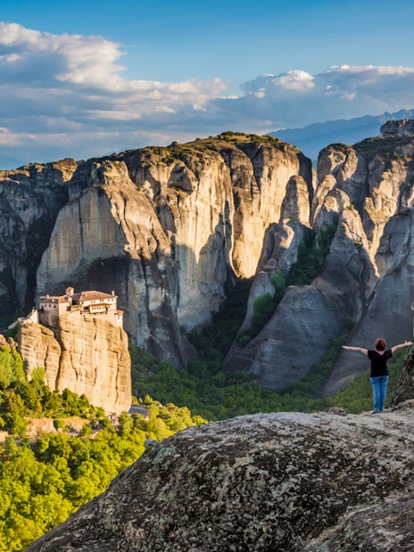 Meteora rock formations with monastery, person standing on cliff, Greece.