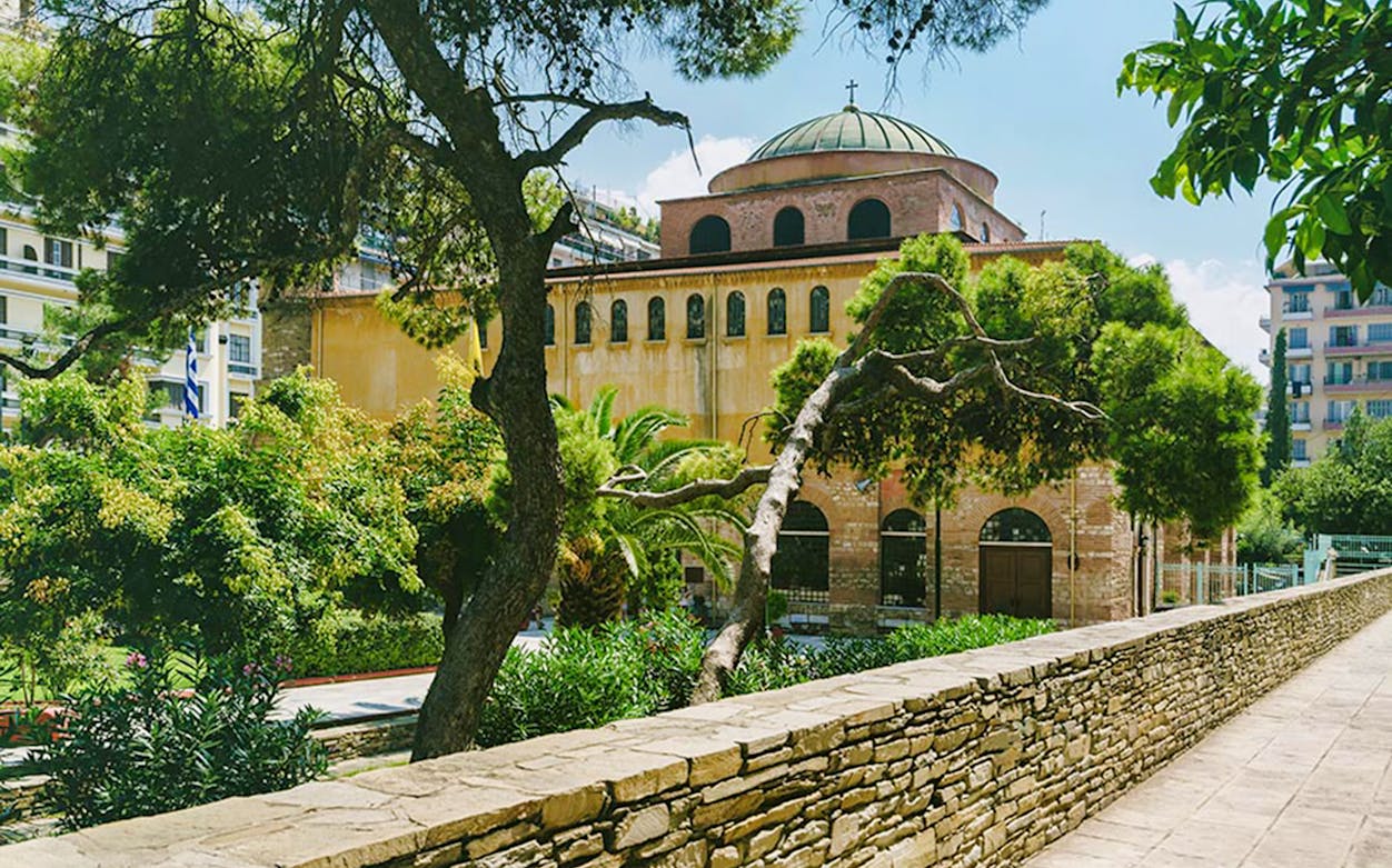 Byzantine church with dome and arched windows in Thessaloniki, surrounded by trees.