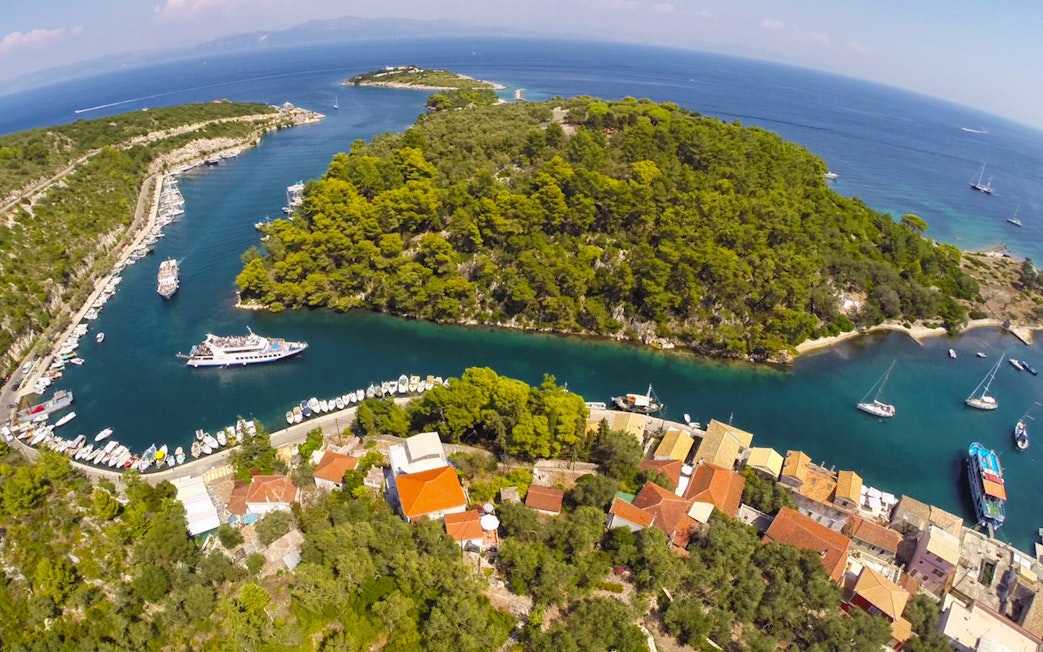 Cruise ship navigating narrow channel near Paxos island, Greece, surrounded by lush greenery and clear blue waters.