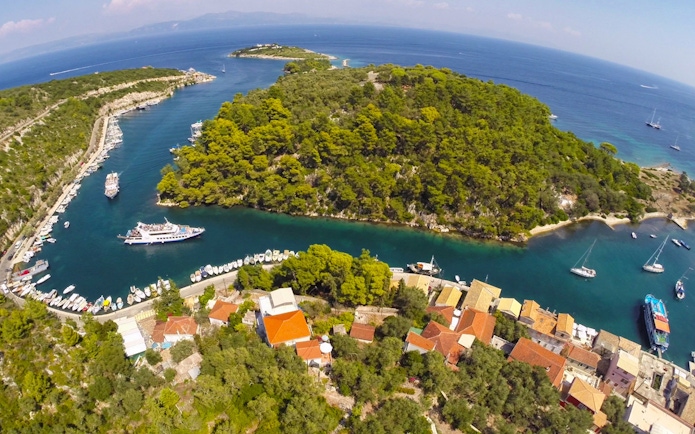 Cruise ship navigating narrow channel near Paxos island, Greece, surrounded by lush greenery and clear blue waters.