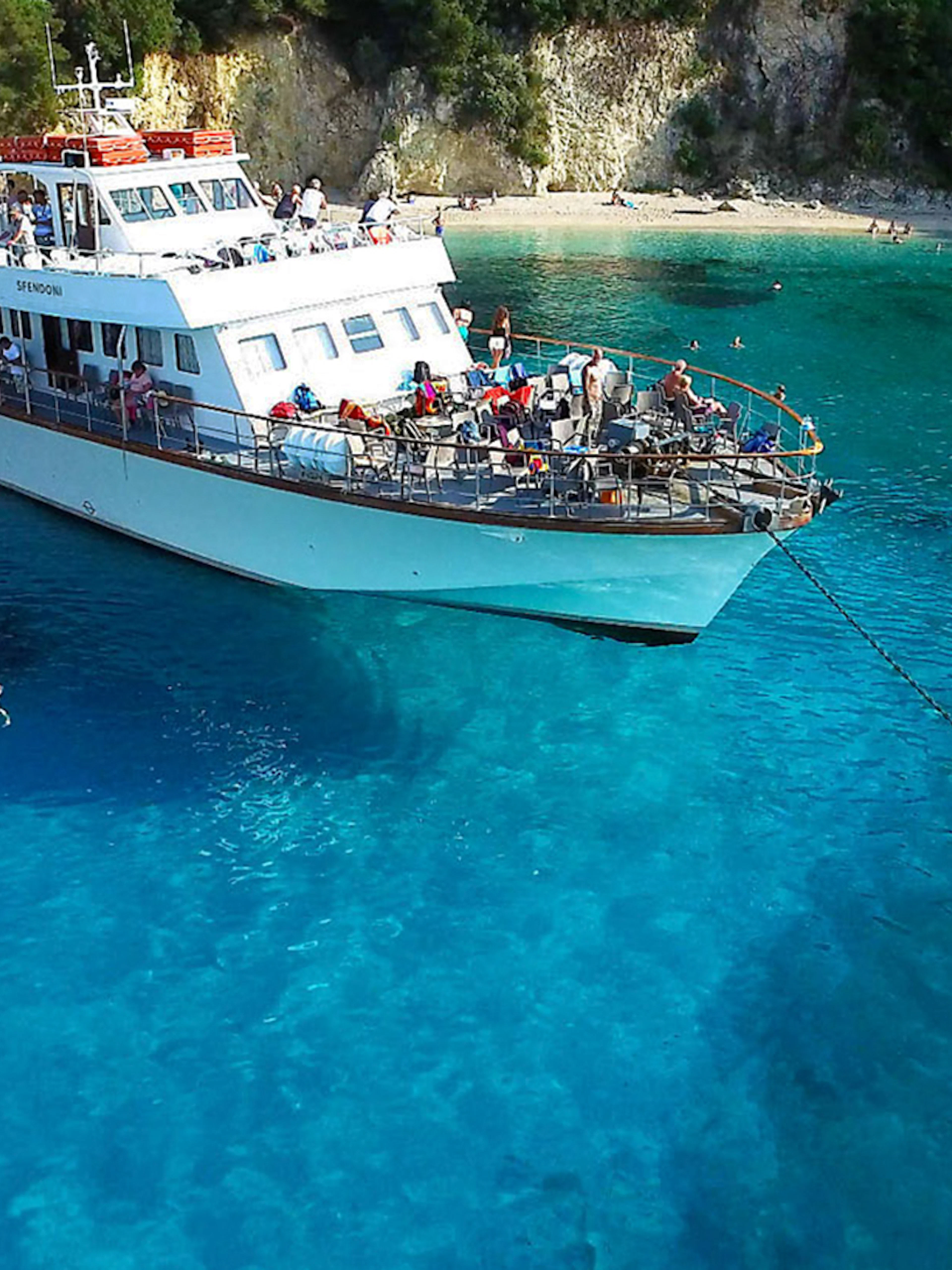 Cruise ship anchored in Blue Lagoon, Corfu, with people swimming nearby.