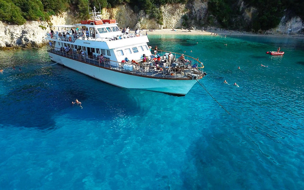 Cruise ship anchored in Blue Lagoon, Corfu, with people swimming nearby.