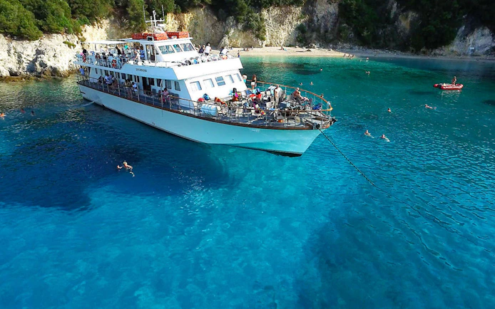 Cruise ship anchored in Blue Lagoon, Corfu, with people swimming nearby.