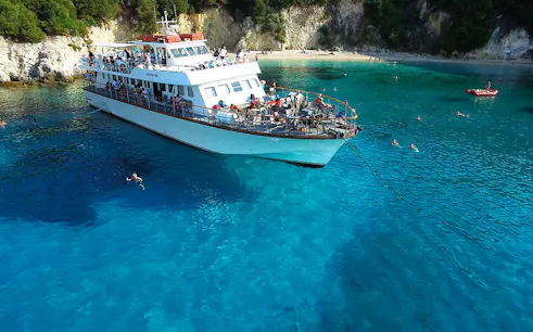 Cruise ship anchored in Blue Lagoon, Corfu, with people swimming nearby.
