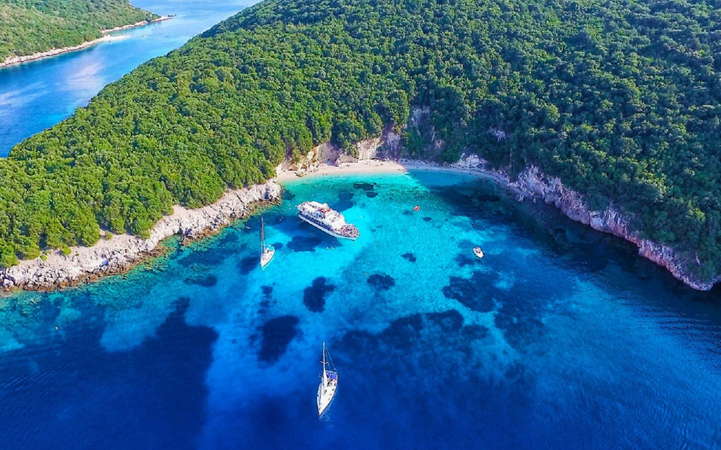 Cruise boats in Blue Lagoon's turquoise waters near Sivota, Corfu, surrounded by lush greenery.