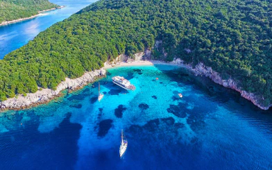 Cruise boats in Blue Lagoon's turquoise waters near Sivota, Corfu, surrounded by lush greenery.