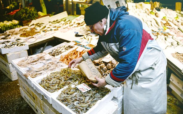 Vendor arranging seafood at Thessaloniki open market during food tasting tour.