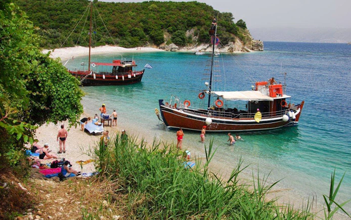 Boat anchored near a beach in Corfu with people enjoying a BBQ and swimming.