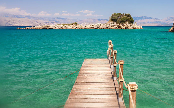 Wooden pier extending into turquoise sea with distant rocky islet, Corfu boat trip.