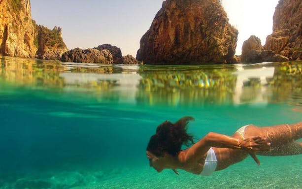 Snorkeler exploring clear waters near rocky cliffs in Corfu during a full-day boat trip with BBQ.
