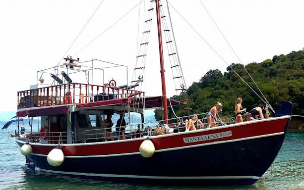 Boat with tourists enjoying a full-day trip in Corfu, Greece, near lush coastline.