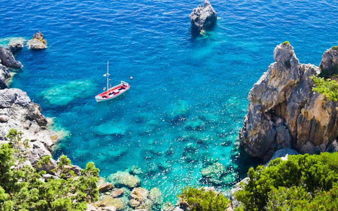 Boat sailing in clear blue waters near rocky coastline in Corfu.
