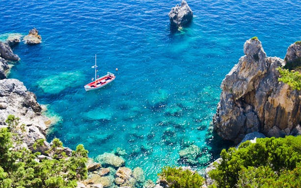 Boat sailing in clear blue waters near rocky coastline in Corfu.