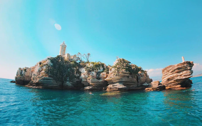 Rocky islet with lighthouse on Corfu boat trip route.