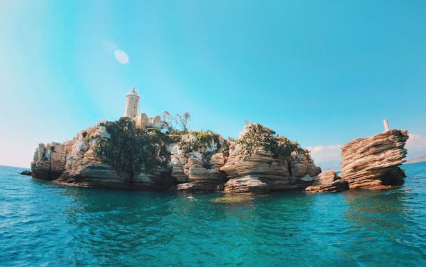 Rocky islet with lighthouse on Corfu boat trip route.