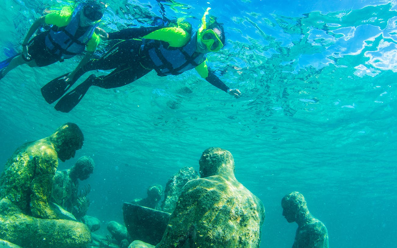 Snorkelers exploring vibrant coral reef and underwater sculptures at MUSA, Cancún.