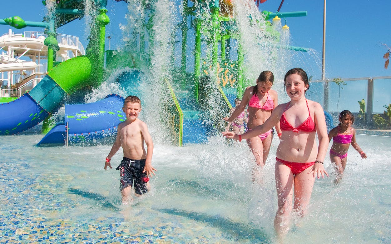 Children playing in water at Aqualava water park with slides in the background.