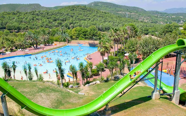 Green water slide and pool at Aqualeon Water Park, Tarragona, with people enjoying the attractions.