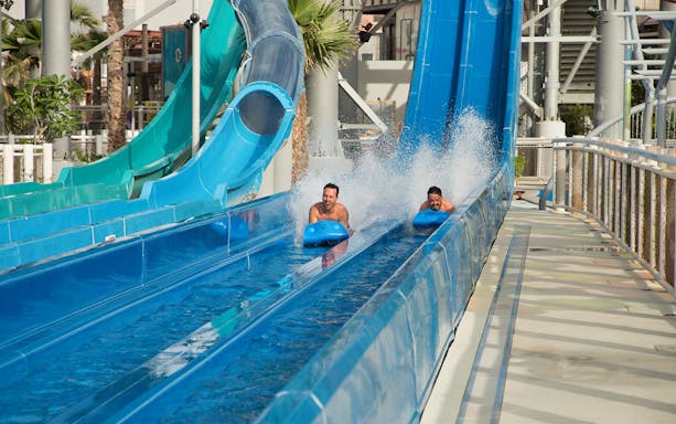 Two people racing on water slides at Laguna Waterpark, Dubai.