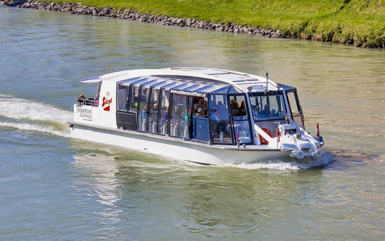 Salzburg river cruise boat on Salzach River with passengers enjoying city views.