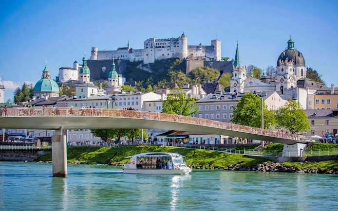 Salzburg city cruise boat on Salzach River with Hohensalzburg Fortress in the background.