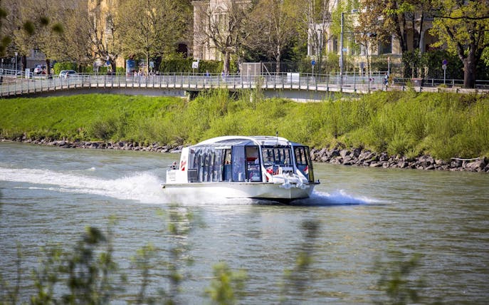 Salzburg river cruise boat on the Salzach River with cityscape in the background.