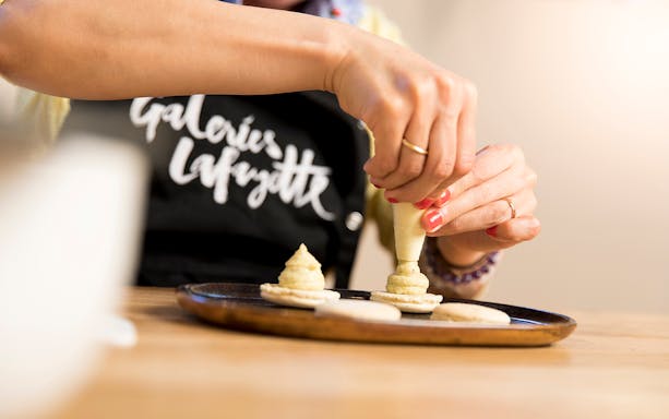 Hands piping filling onto macarons during family macaron class in Paris.