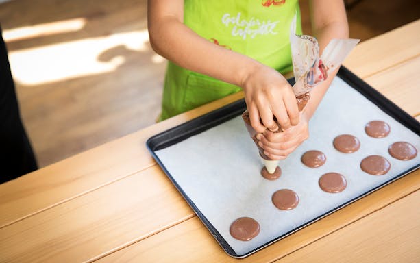 Piping chocolate macaron batter onto a baking sheet during a family macaron class.