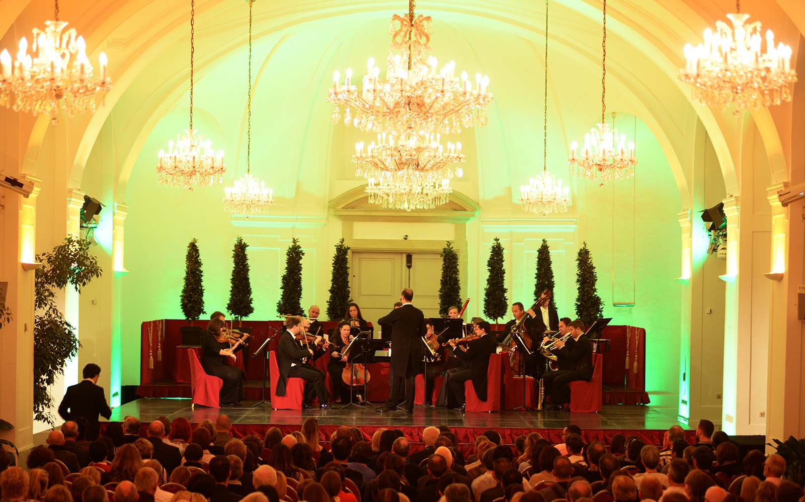 Orchestra performing at Schönbrunn Palace concert hall, Vienna, with audience seated.