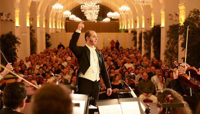 Conductor leading orchestra at Schonbrunn Palace concert in Vienna, audience enjoying music.