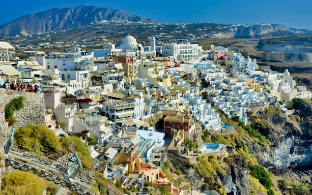 Santorini cable car descending with view of Fira's white buildings and Aegean Sea backdrop.