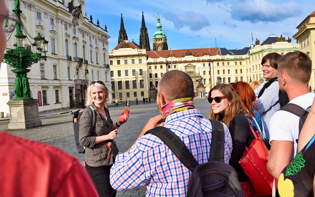 Tour group at Prague Castle courtyard with guide, spires in background.