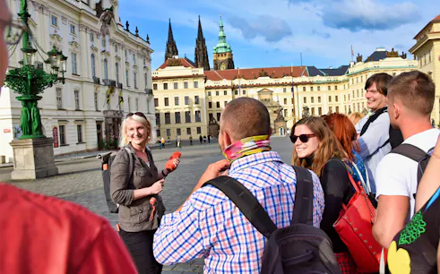 Tour group at Prague Castle courtyard with guide, spires in background.