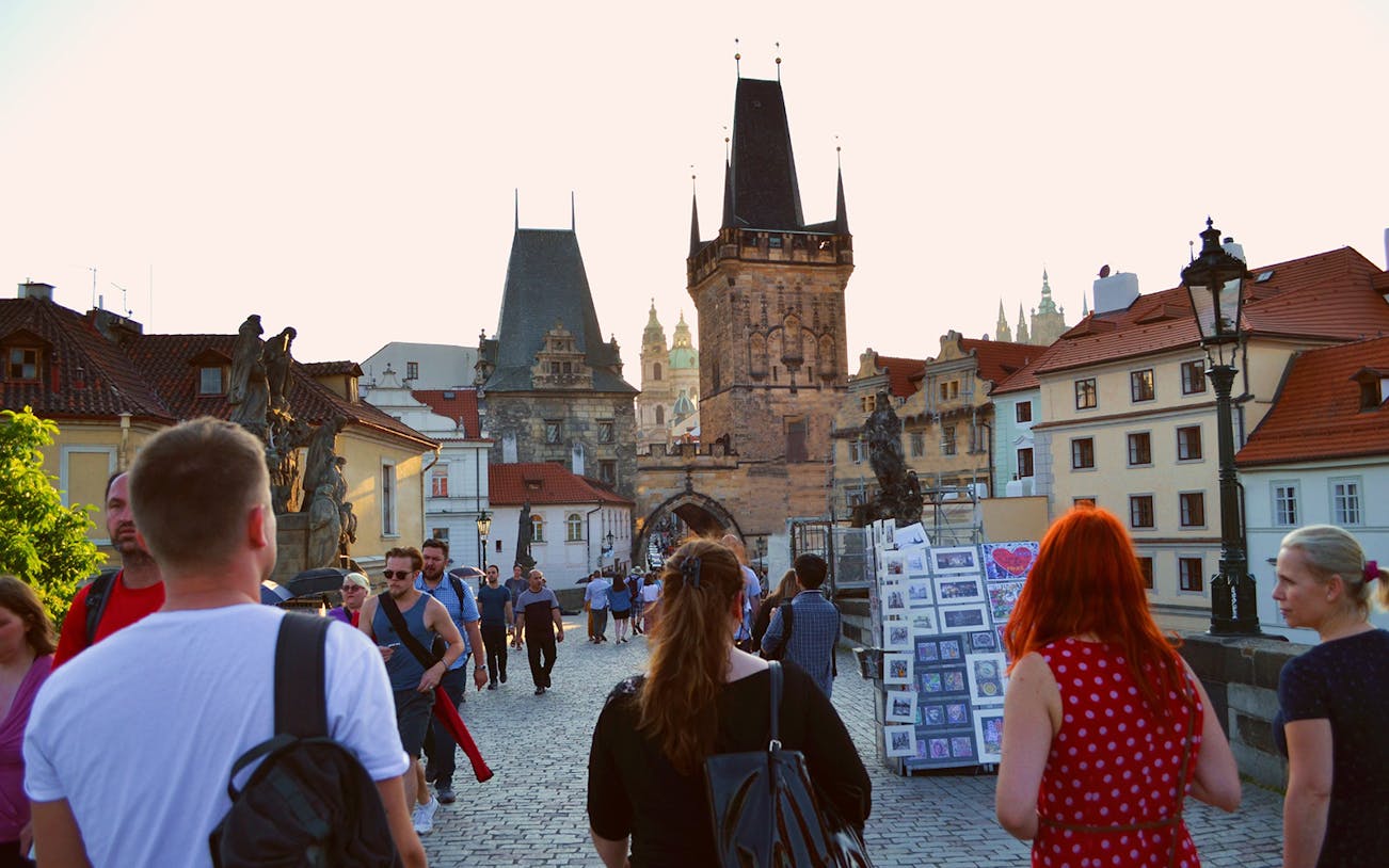 Evening walk on Charles Bridge, Prague, with view of Gothic towers and street vendors.